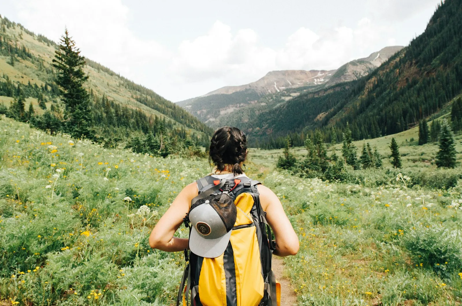 Traveler with a yellow backpack walking through a green mountain valley