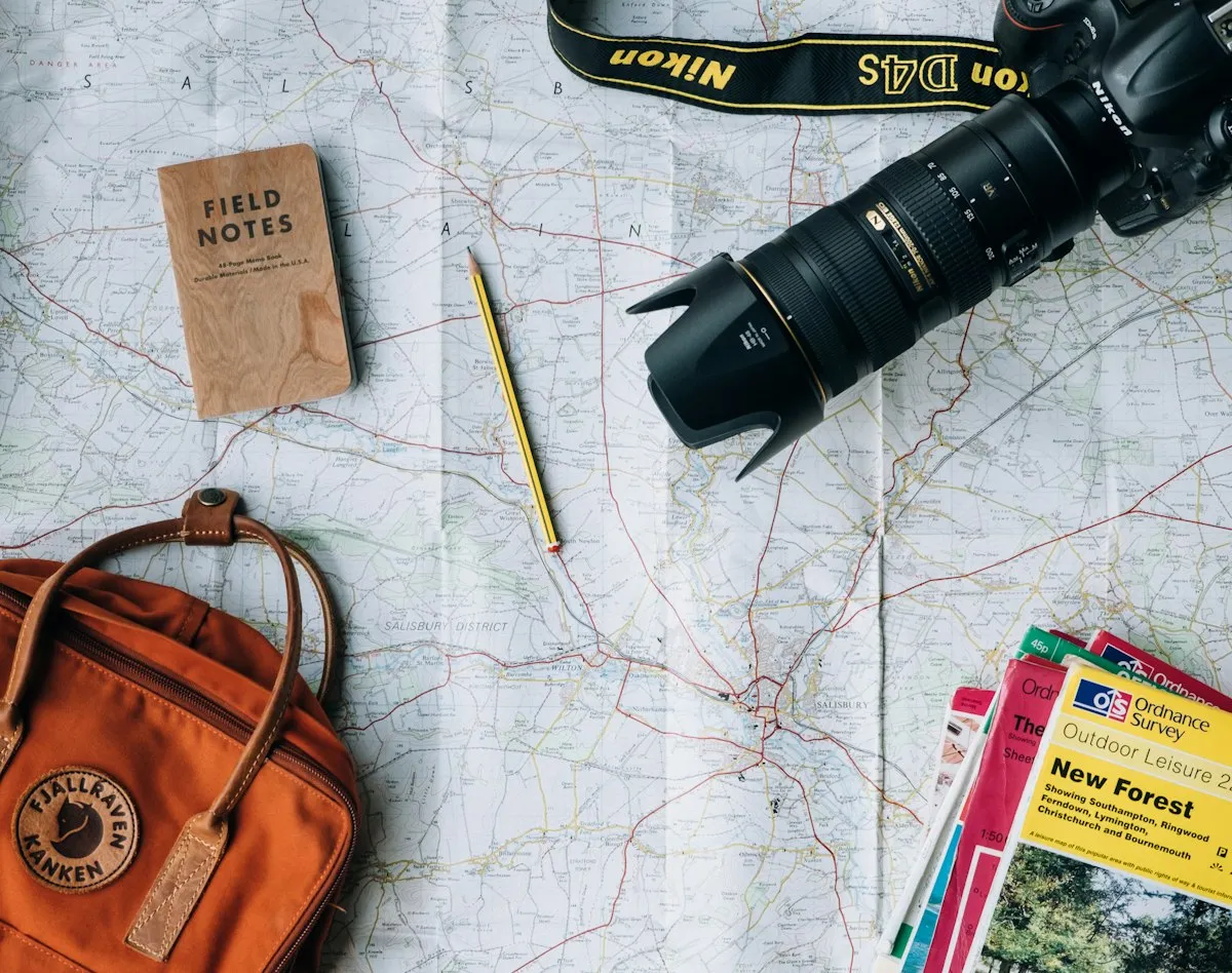 Travel essentials, a paper map, camera and backpack laid out on a table